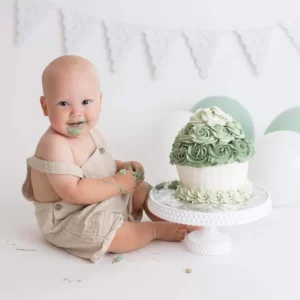 Glad kille som smashar grön tårta under en 1årsfotografering