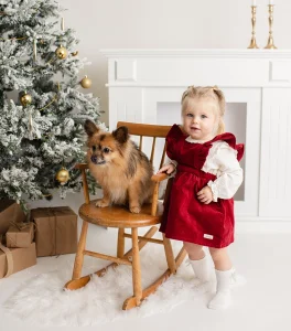 Ett julkort med barn och hund i en fotostudio framför en julgran och öppen spis. 