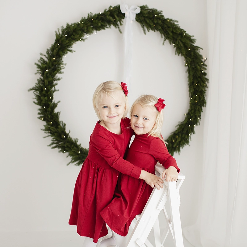 Julkortsfotografering i studio med två tjejer i röd klänning framför en stor julkrans.