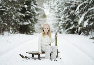 Novalie med Silver Russel Syndrom blir fotograferad på en släde i en vintrig skog.