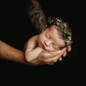 Nyföddfotografering med en liten bebis i pappas händer.